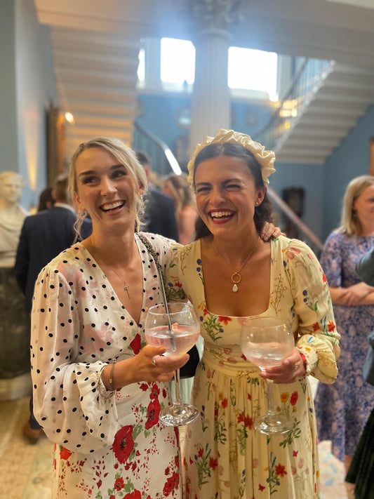 Madeleine and her friend at a wedding wearing a gold and pearl necklace.