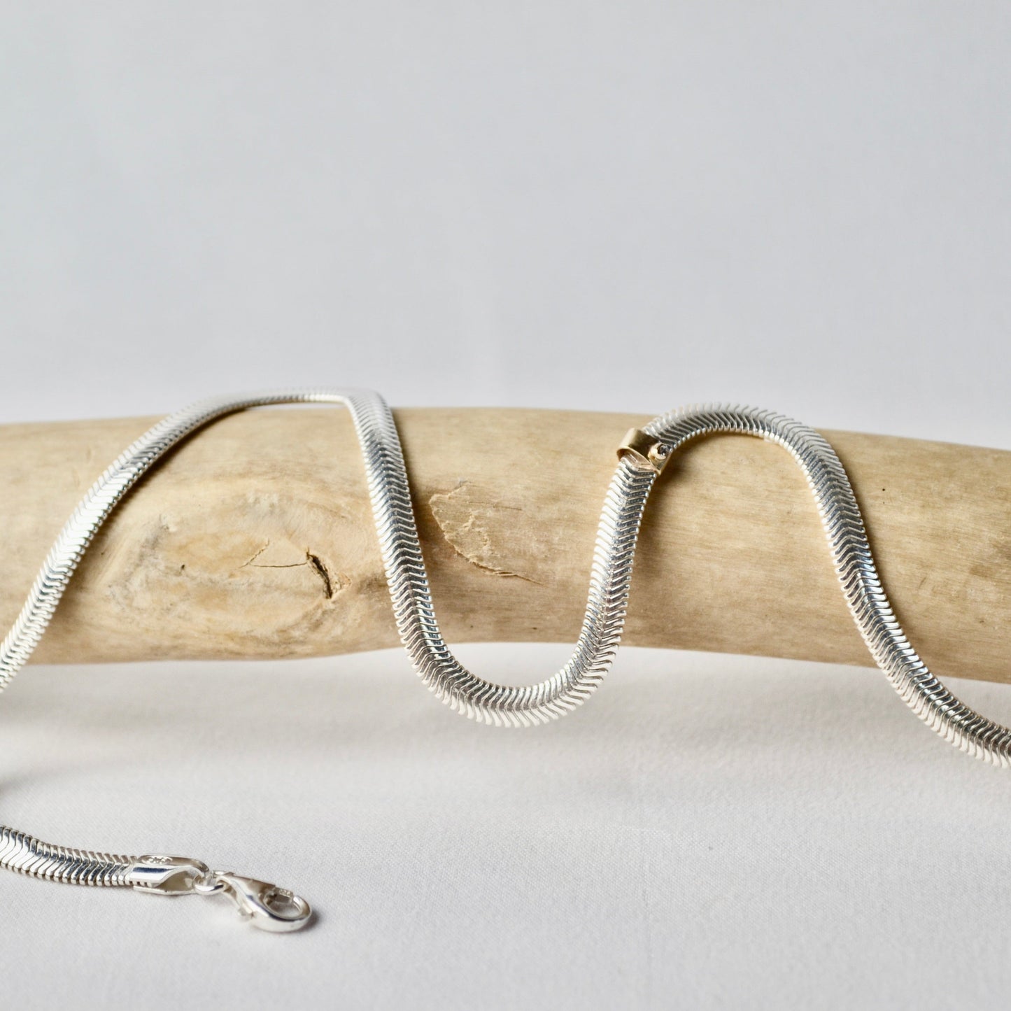 Silver chain necklace on a wooden stick with a light gray background