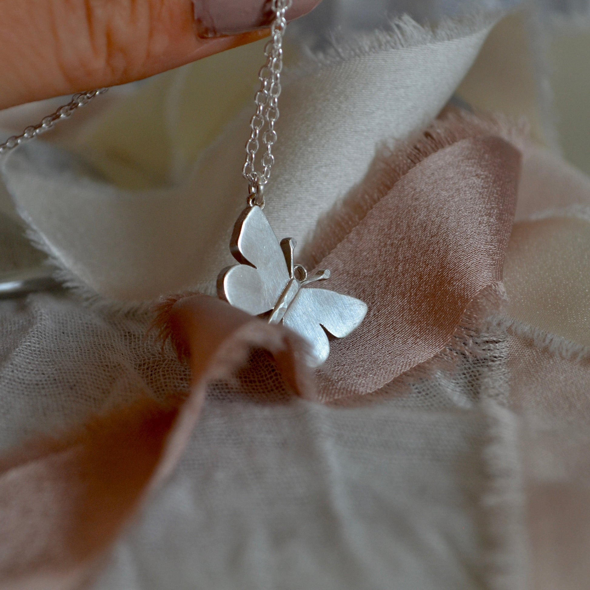 Silver butterfly necklace held over a textured beige fabric background