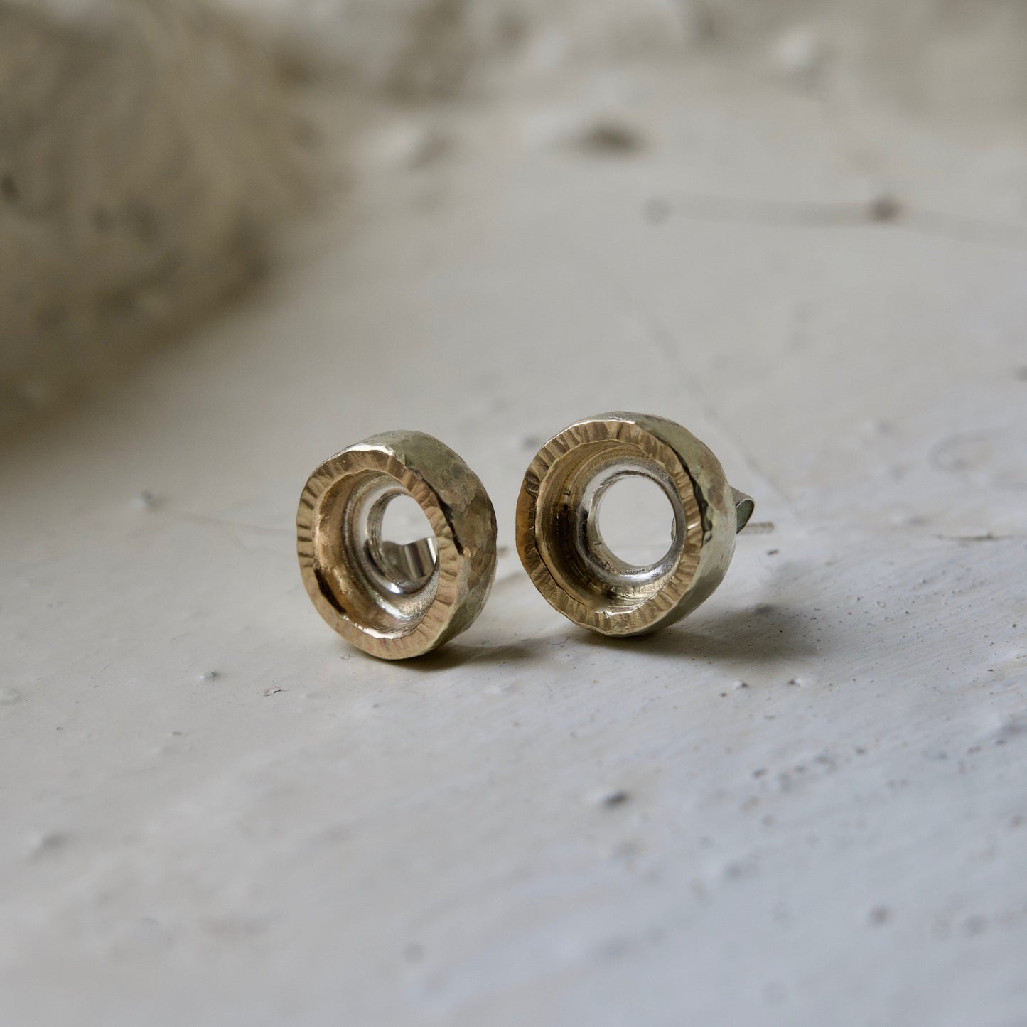 A pair of gold and silver carousel stud earrings placed on a textured surface.