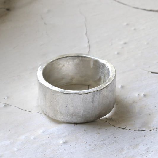 A chunky, flat, silver ring on a textured surface, possibly a sterling silver band ring.