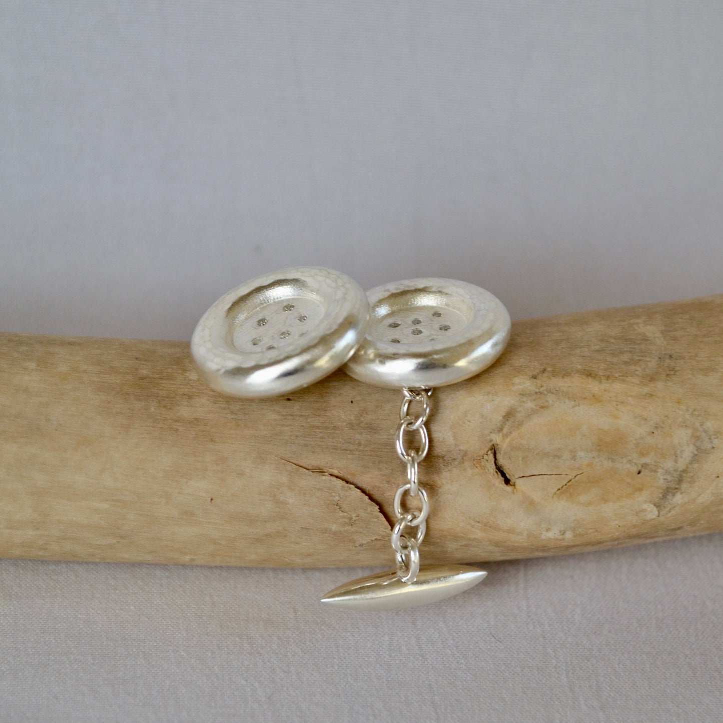 Silver button earrings on a piece of wood with a gray background