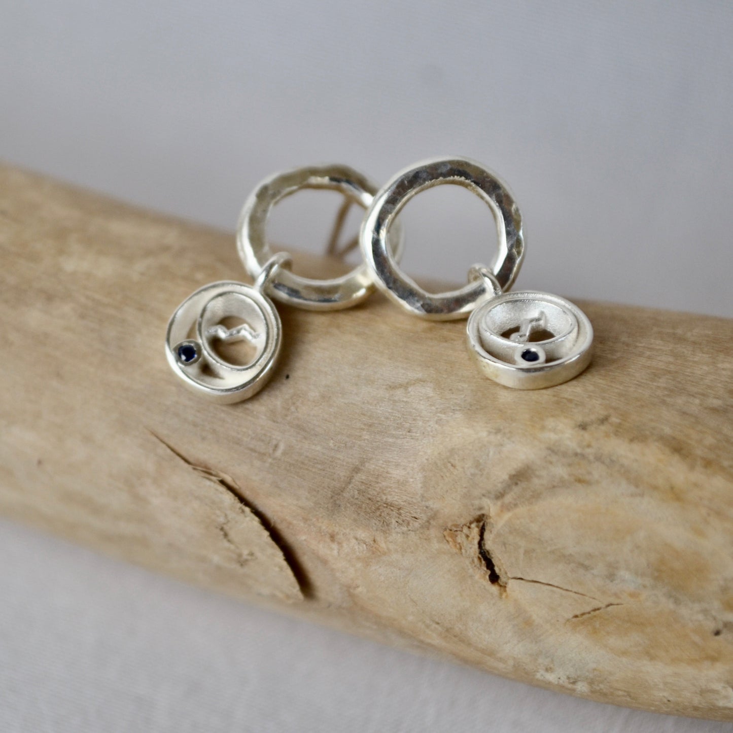 Silver earrings on a piece of driftwood with a neutral background