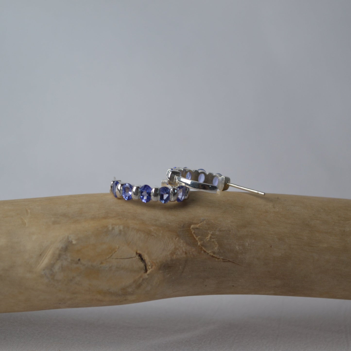 Silver hoop earrings with blue gemstones on a wooden branch against a gray background