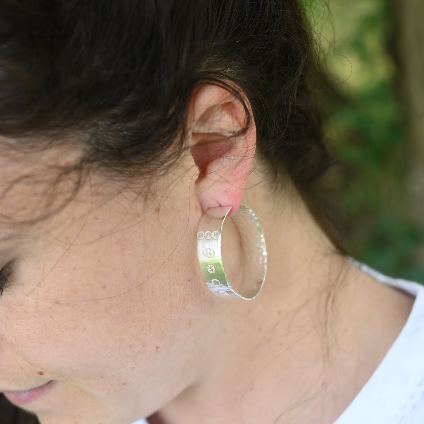 madeleine wearing handmade silver hoops, hallmarked. In the garden.