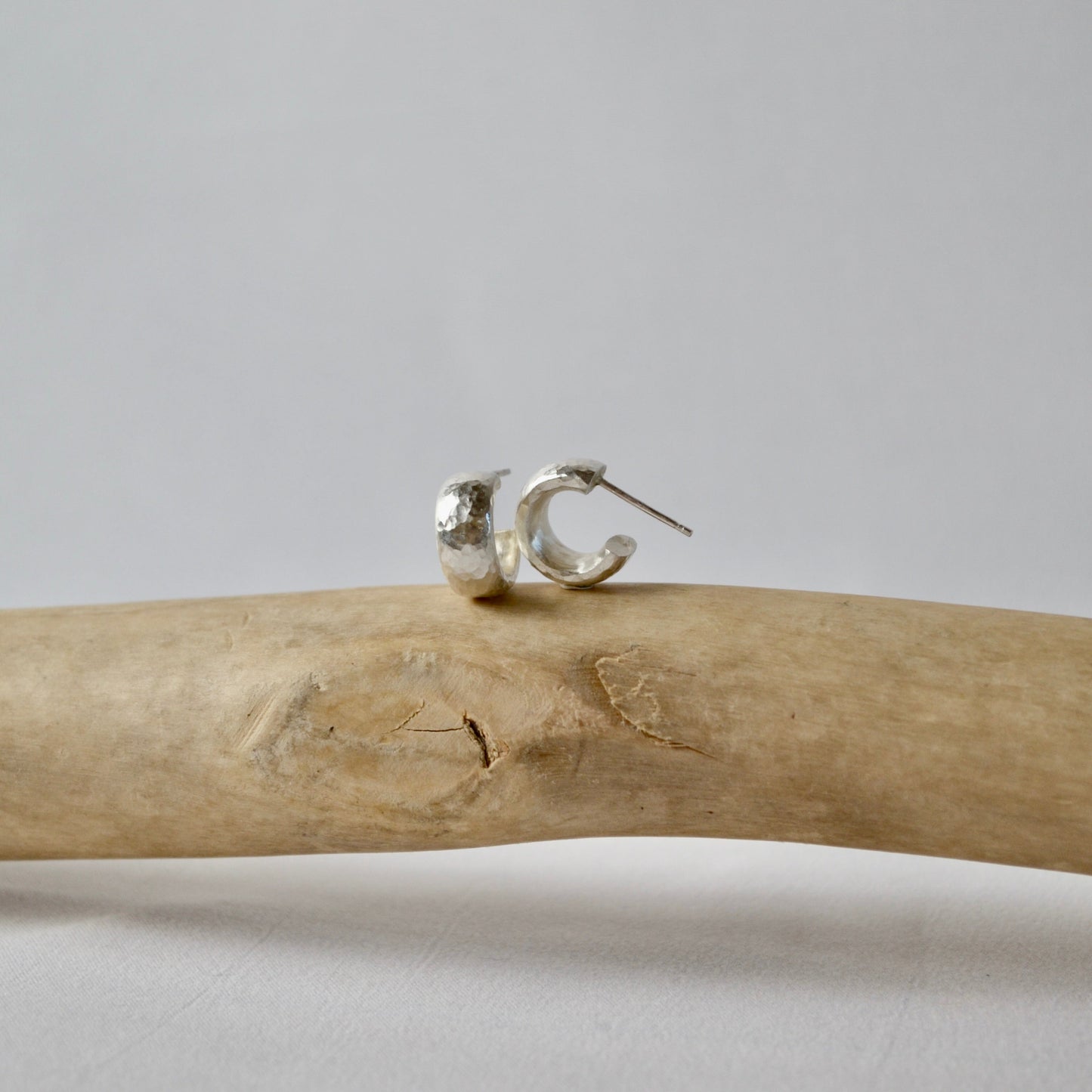 Silver hoop earrings on a piece of driftwood with a gray background