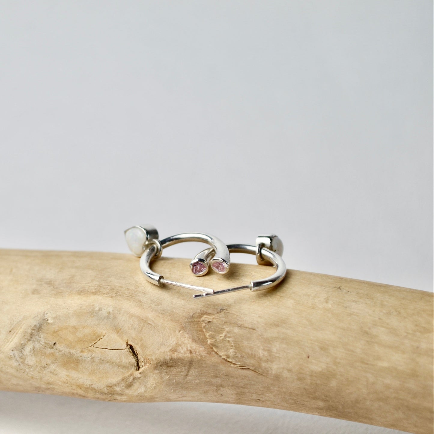 Two silver rings with small stones on a wooden stick against a light gray background