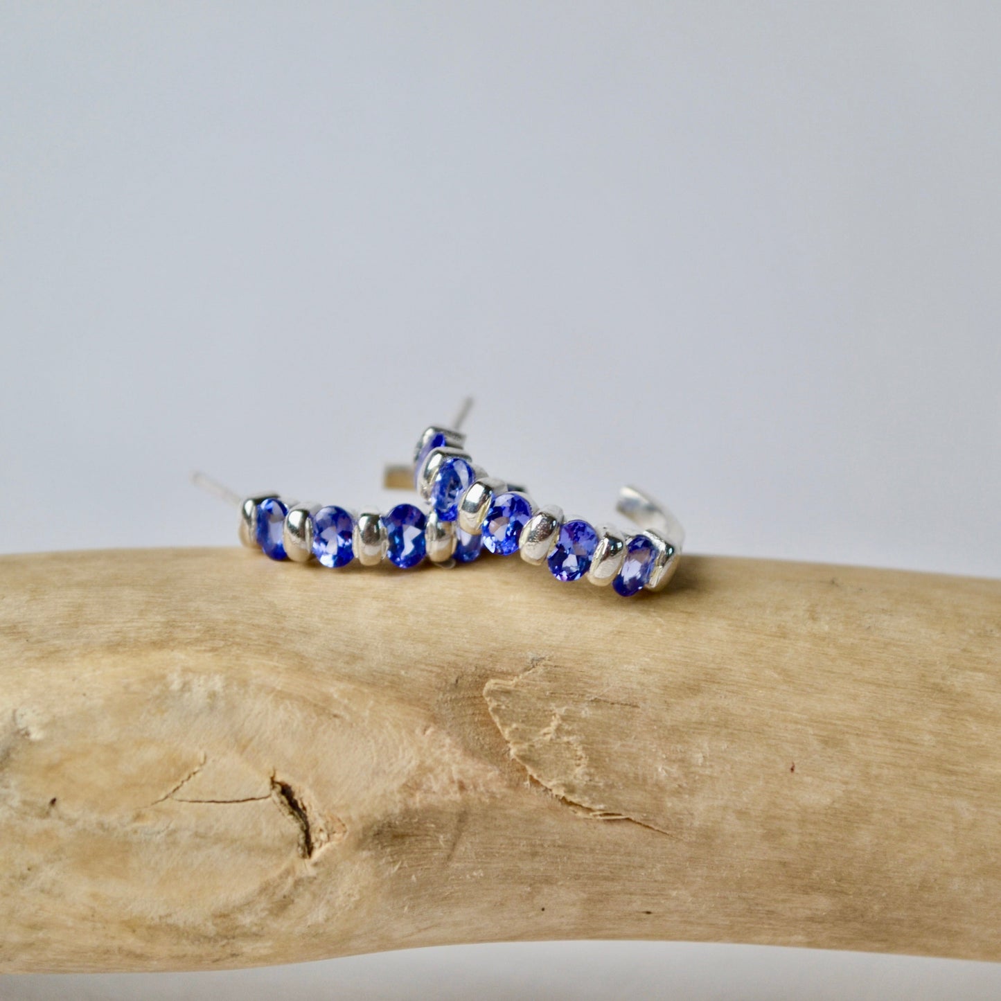Bracelet with blue and silver beads on a piece of driftwood against a light gray background