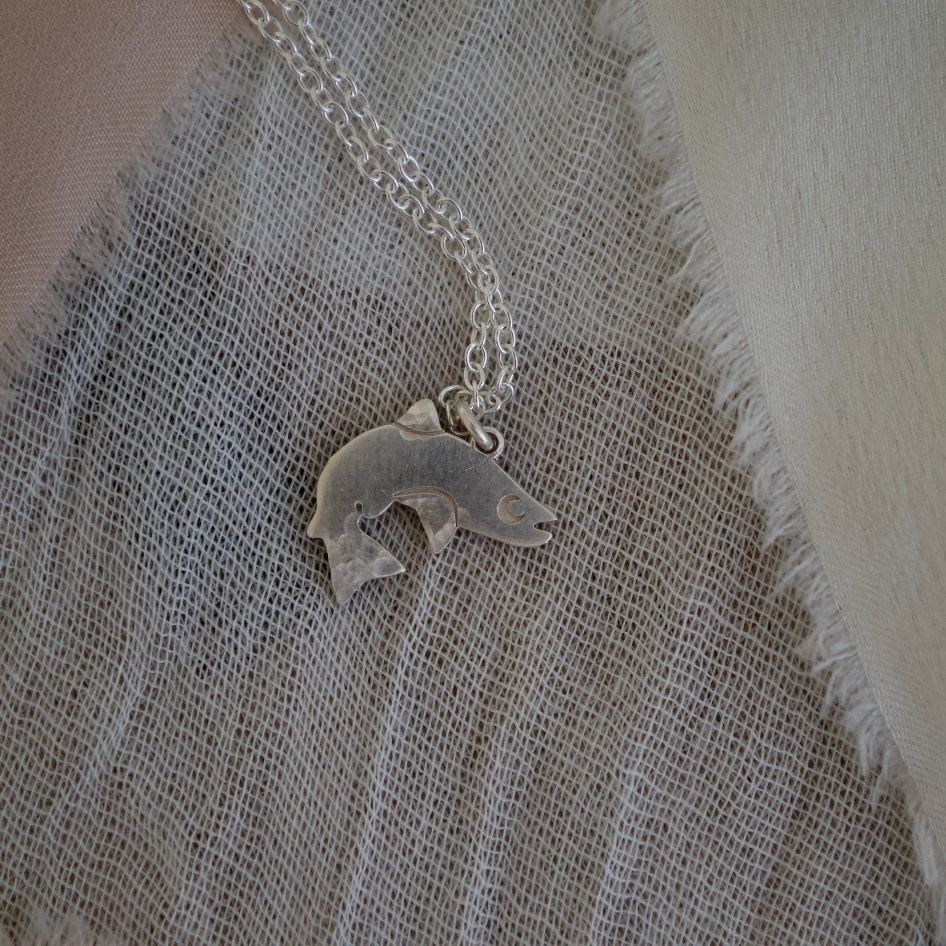 Silver salmon pendant necklace on a textured fabric background