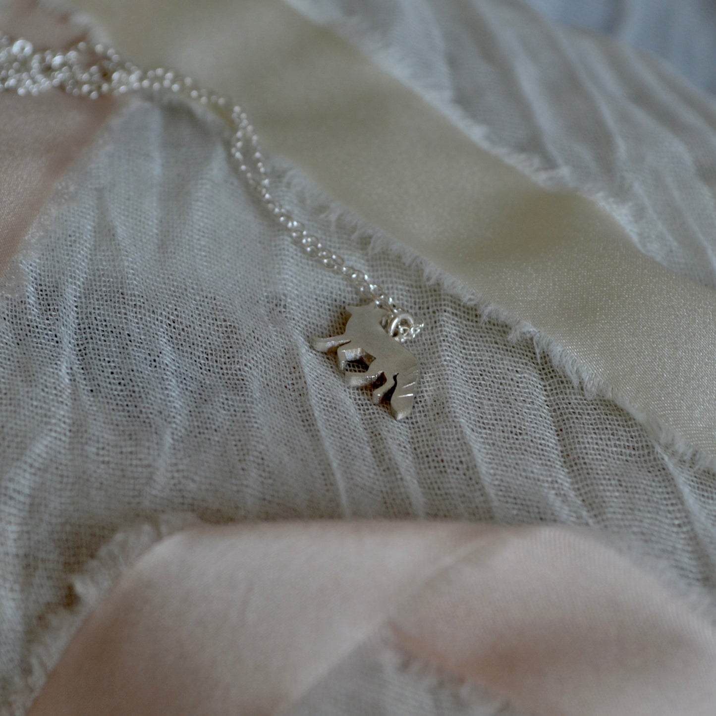Silver necklace with a pendant on a textured beige fabric background