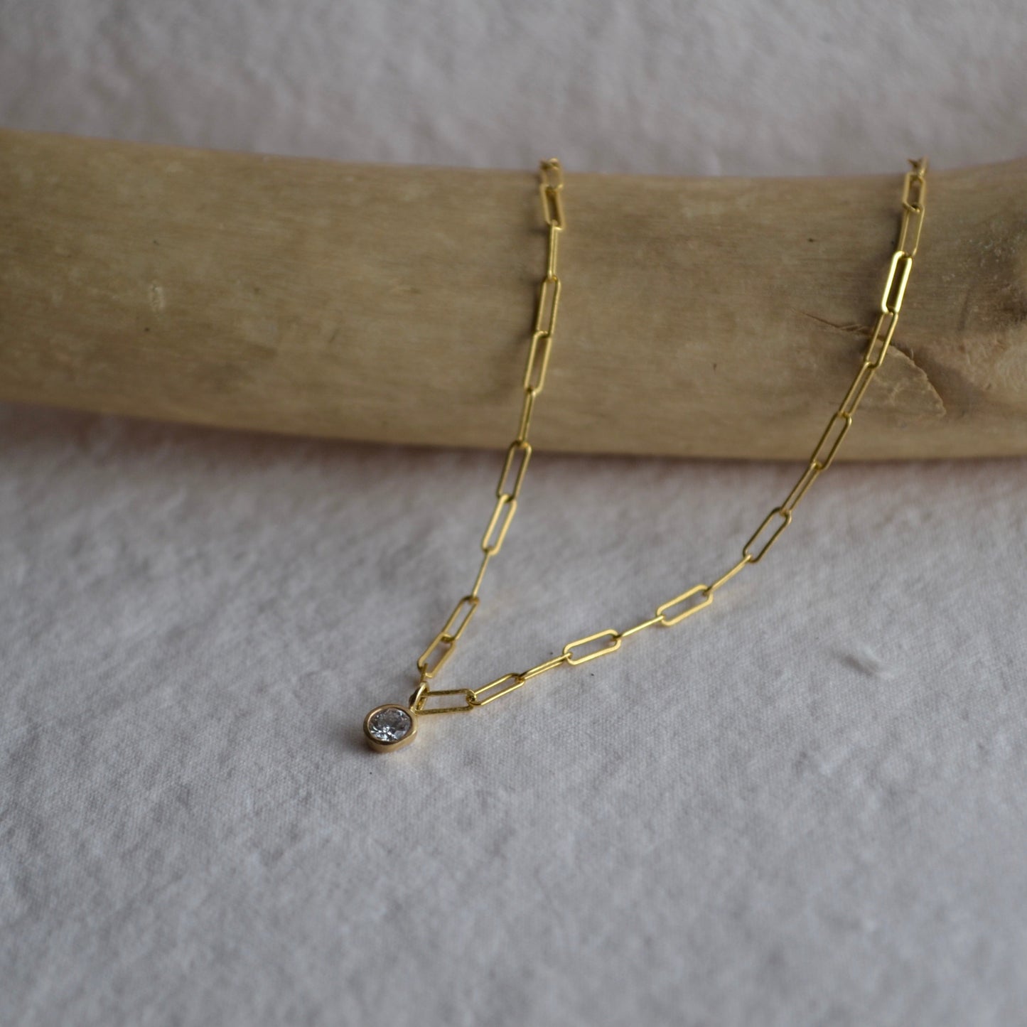 Gold chain necklace with a small pendant on a wooden stick against a light background