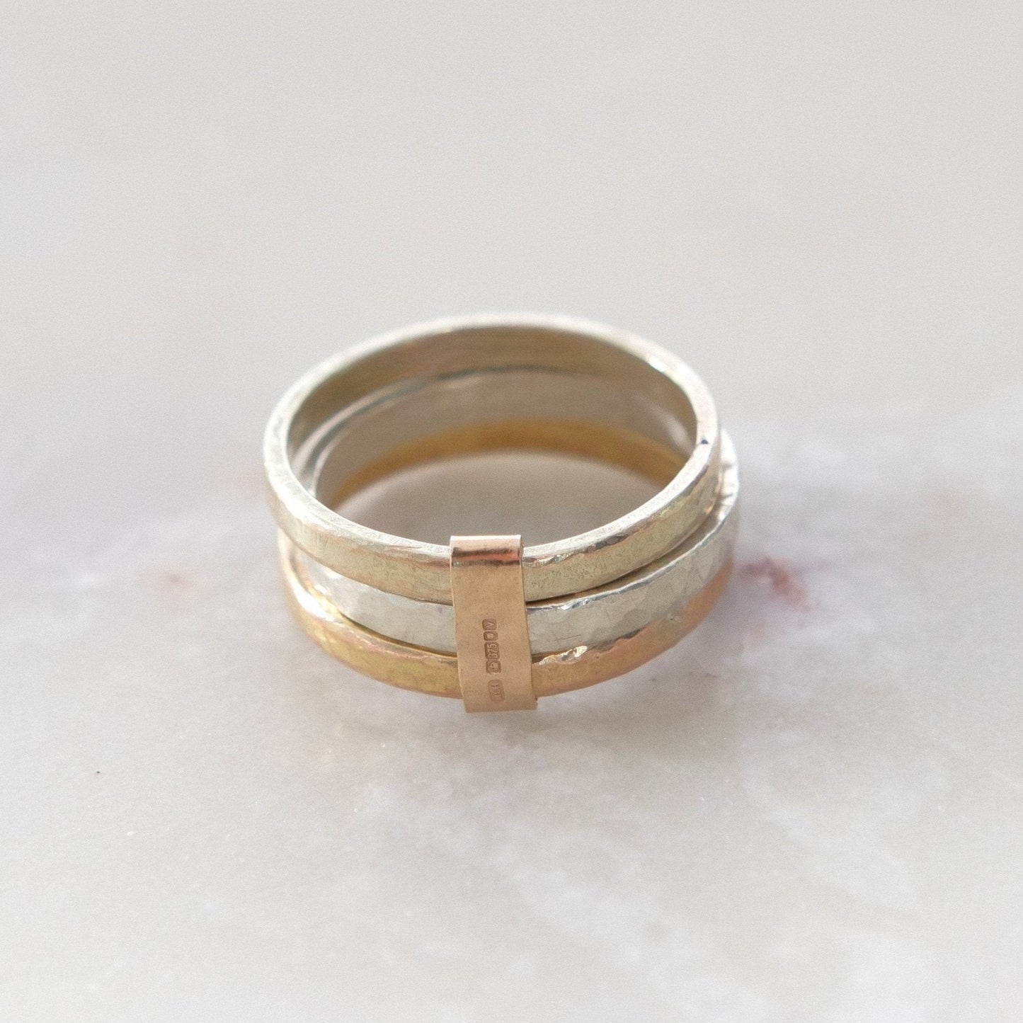 Three stacked 9ct gold rings on a marble surface, with a slim yellow gold link connecting them.