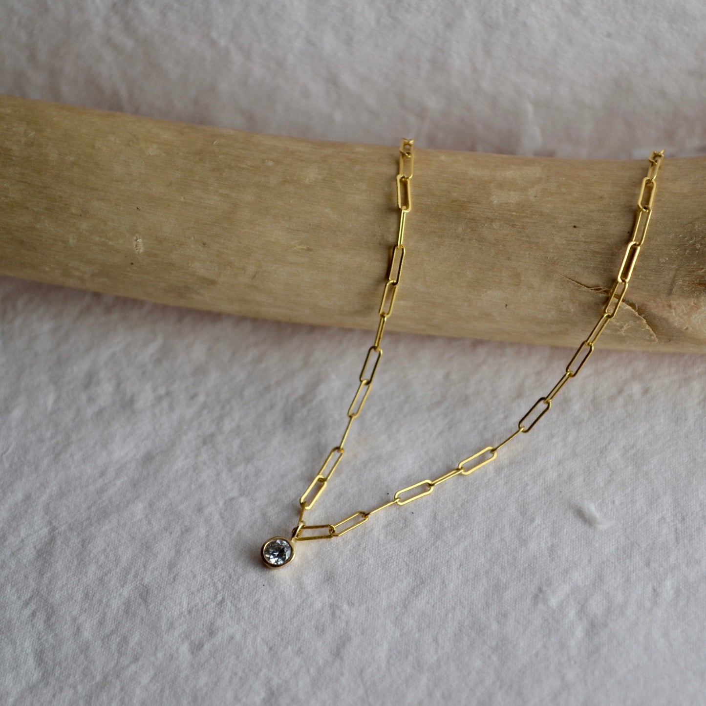 Gold chain necklace with a small pendant on a wooden stick against a white background