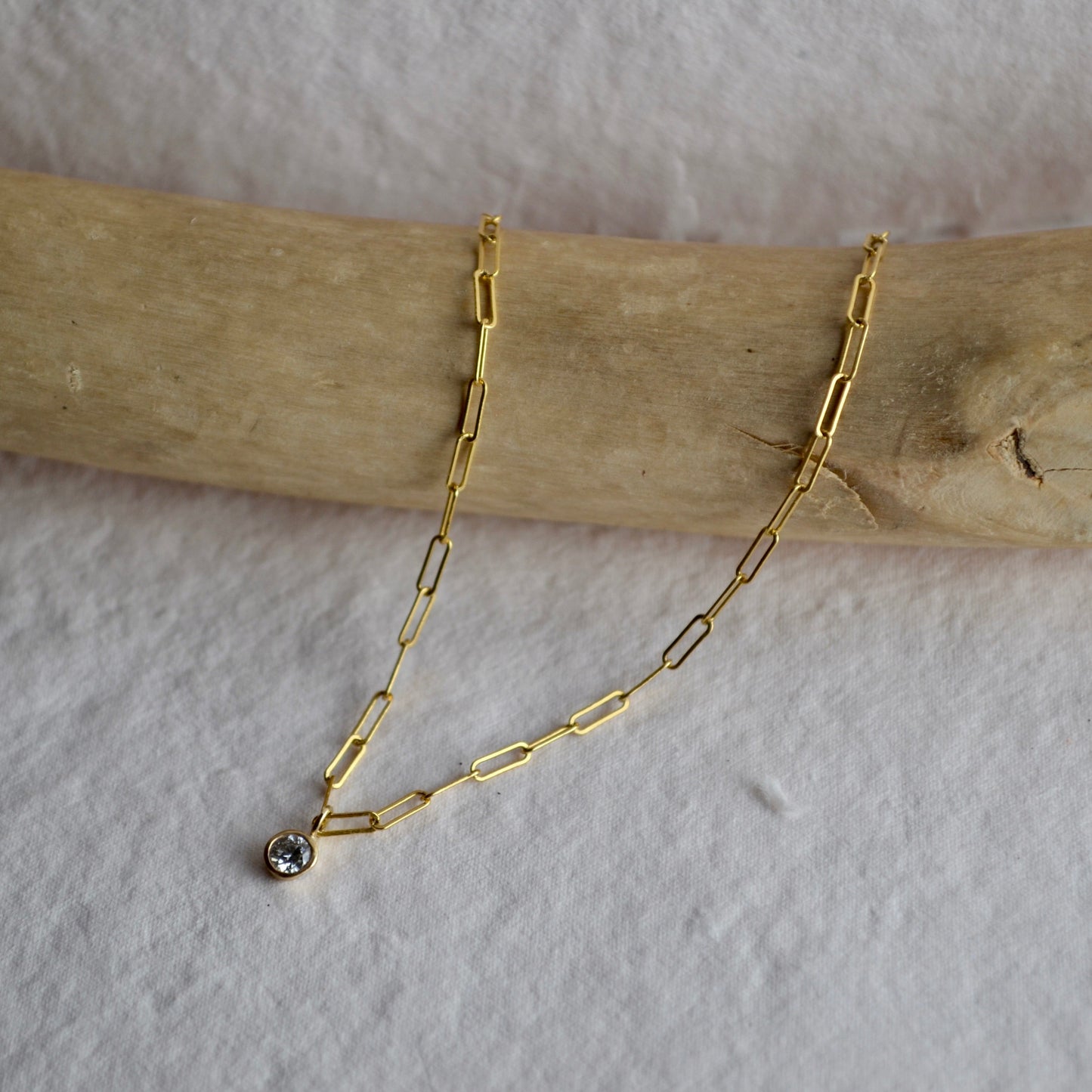 Gold chain necklace with a small pendant on a wooden stick against a white background