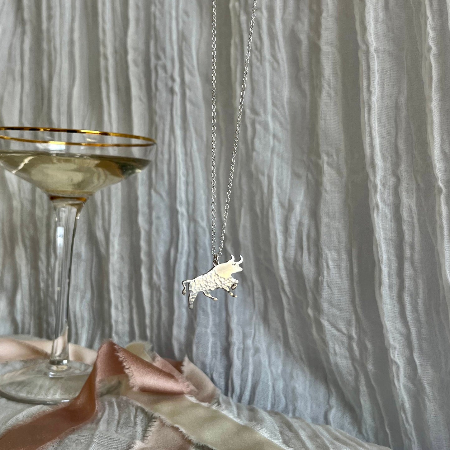Necklace with a unicorn pendant next to a glass of champagne on a textured surface