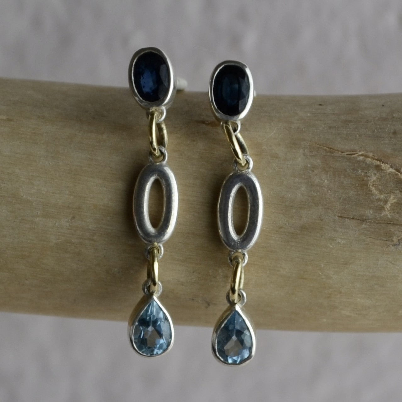 Silver earrings with blue gemstones on a wooden stick