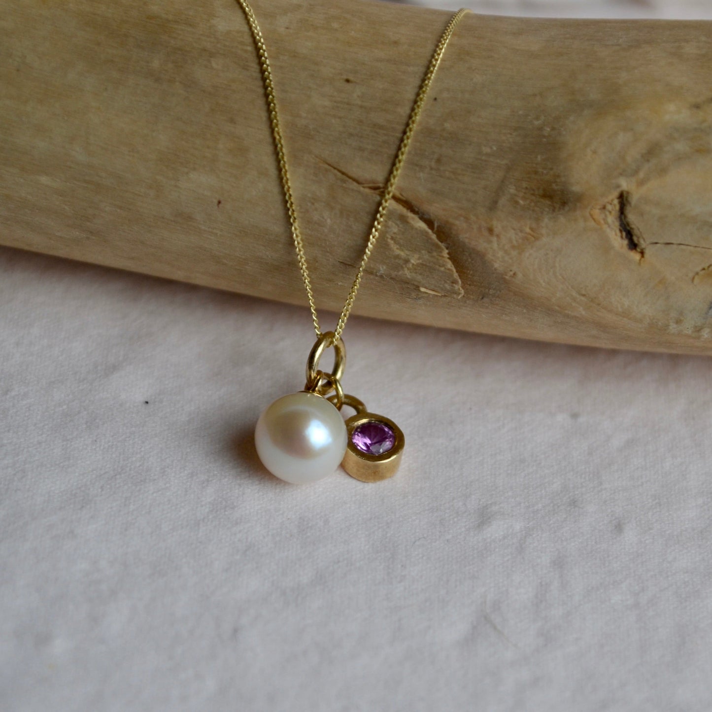Gold necklace with a pearl and gemstone pendant on a wooden surface