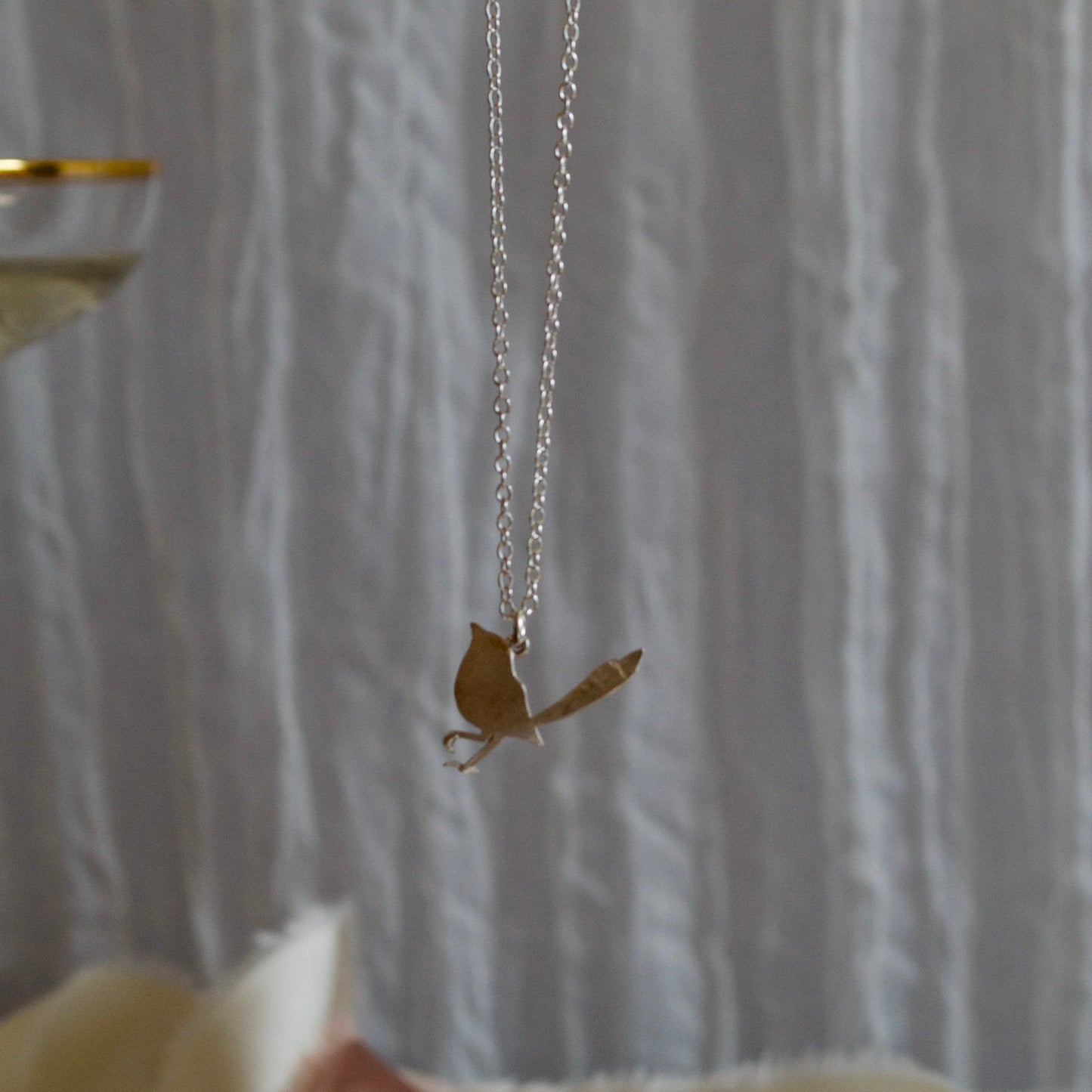 Robin pendant necklace held by a hand against a textured white background