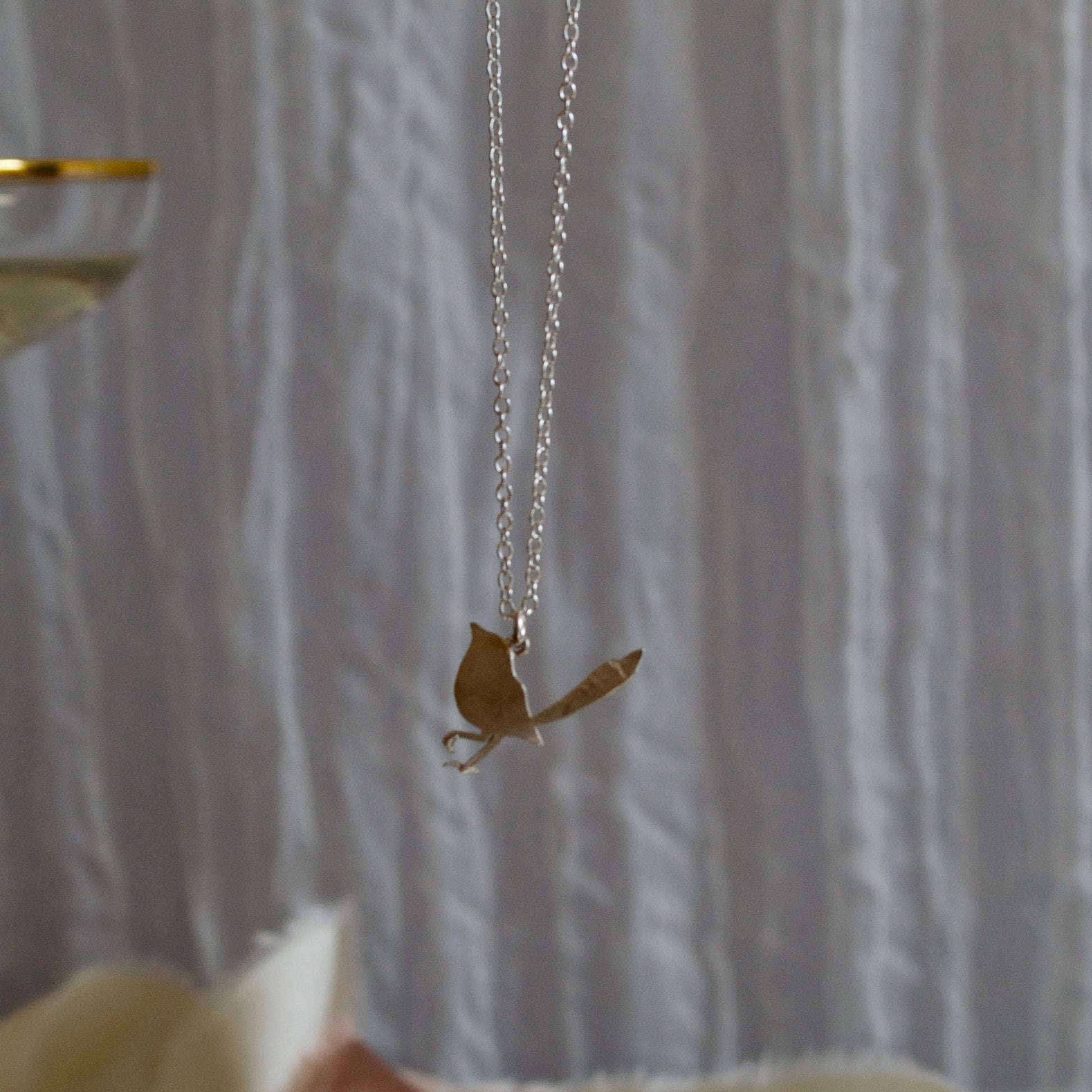 Robin pendant necklace held by a hand against a textured white background