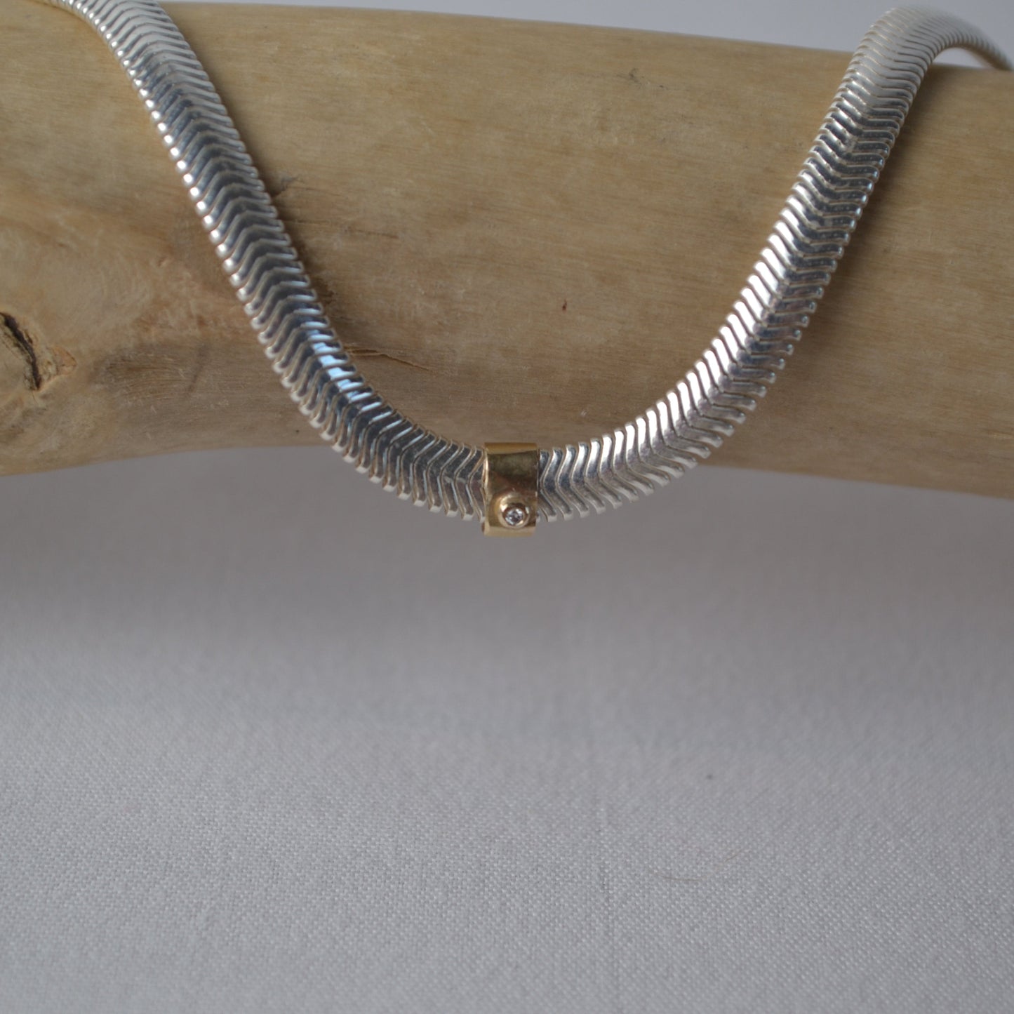 Silver snake chain necklace with a gold clasp on a wooden surface