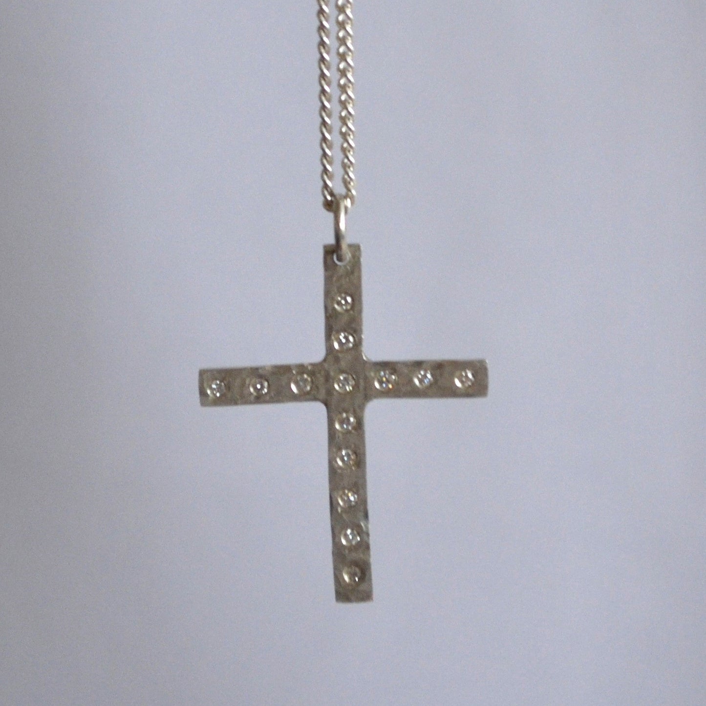 Silver cross necklace with small stones on a light gray background