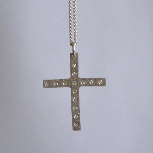 Silver cross necklace with small stones on a light gray background