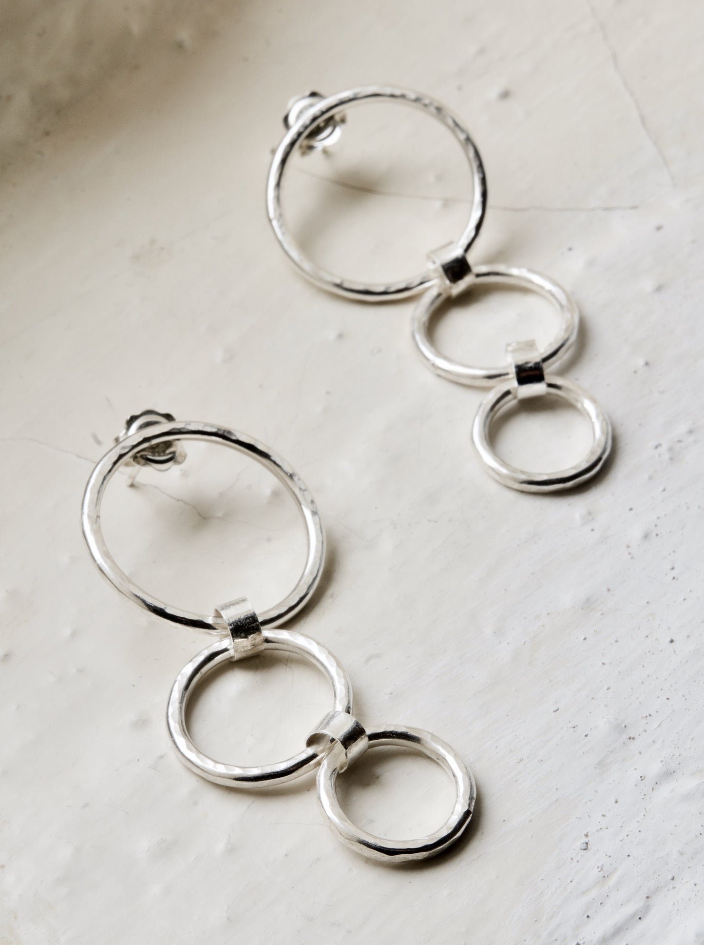 A pair of silver hoop earrings with ascending circles design, laid on a white surface.