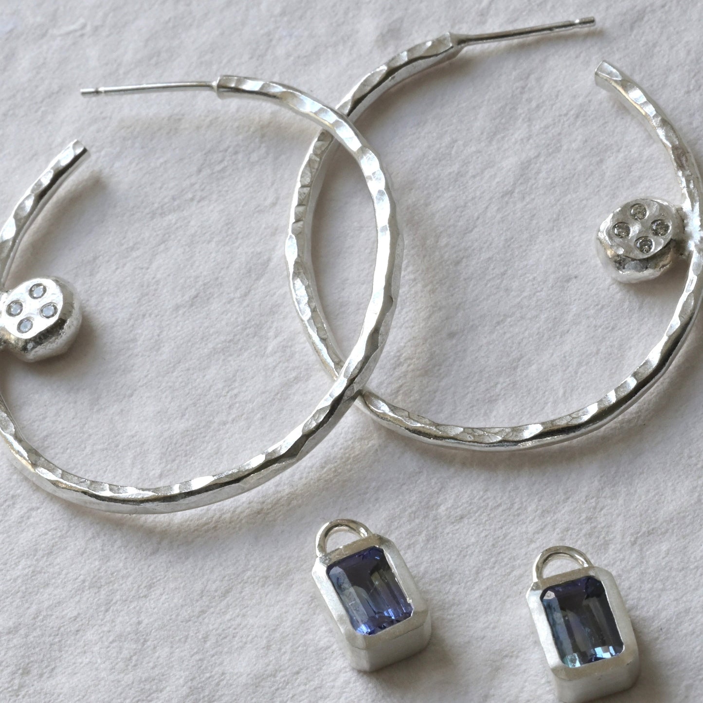 A pair of tanzanite and sterling silver hoops with diamond photographed on white. Handmade fine jewellery by Madeleine.