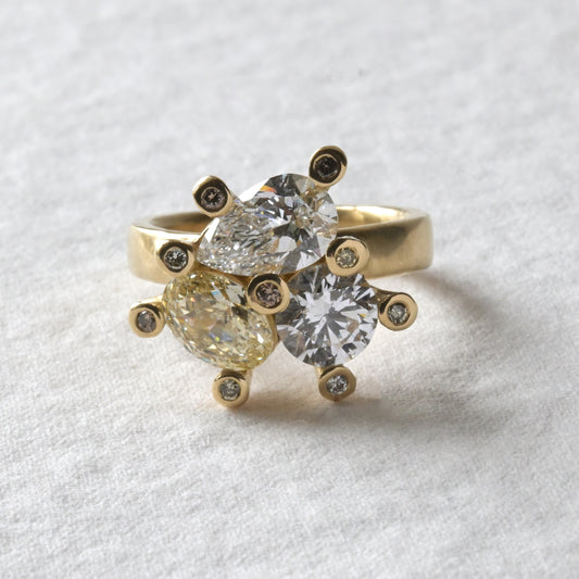 An 18ct yellow gold engagement ring with a central cluster of three uniquely shaped diamonds, surrounded by smaller yellow diamonds set in claws.