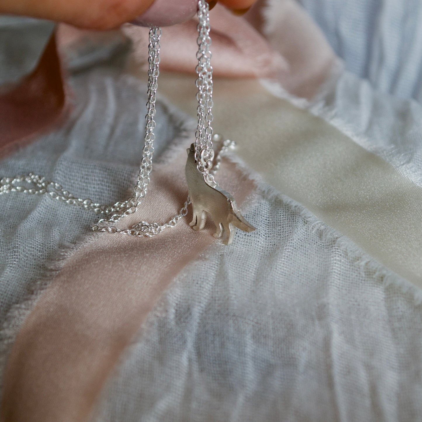 Hand holding a silver necklace with a small animal pendant on a light fabric background
