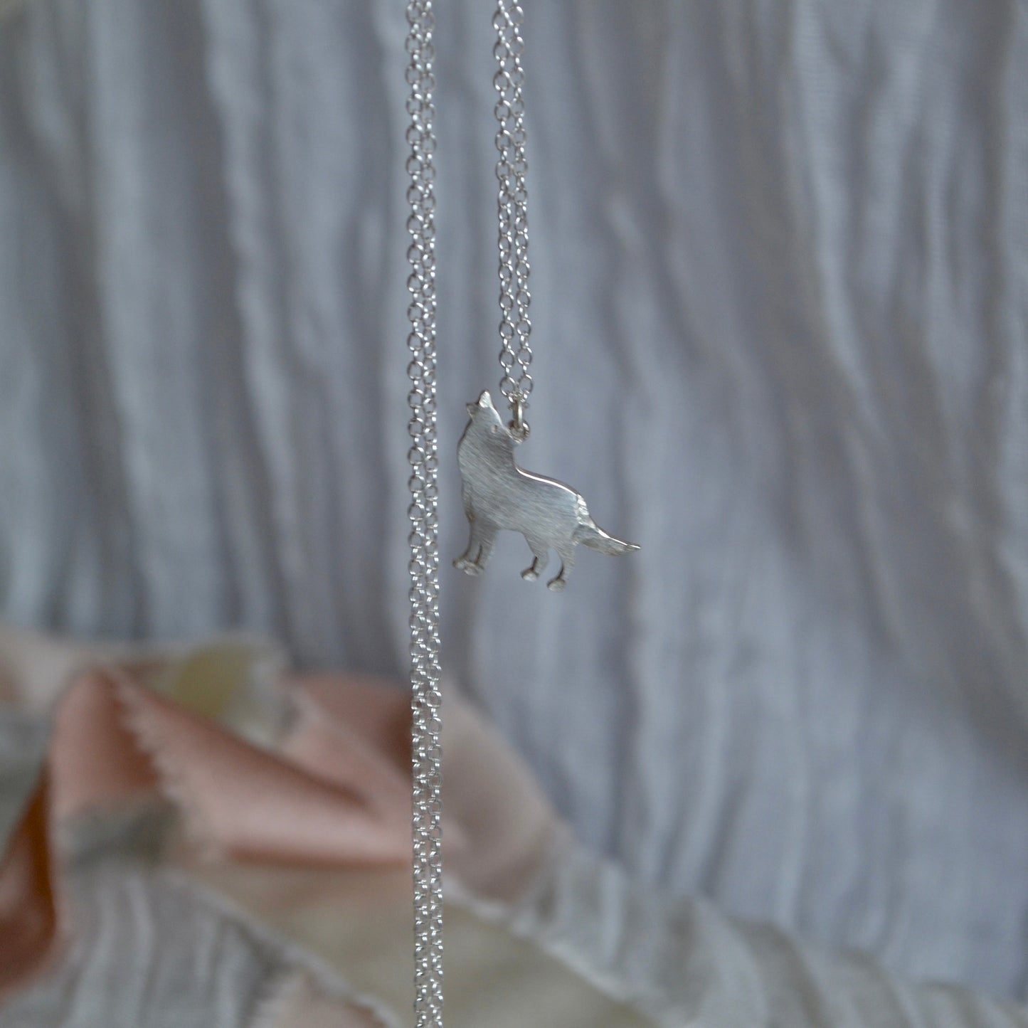 Silver necklace with a small animal pendant held by a hand against a neutral background