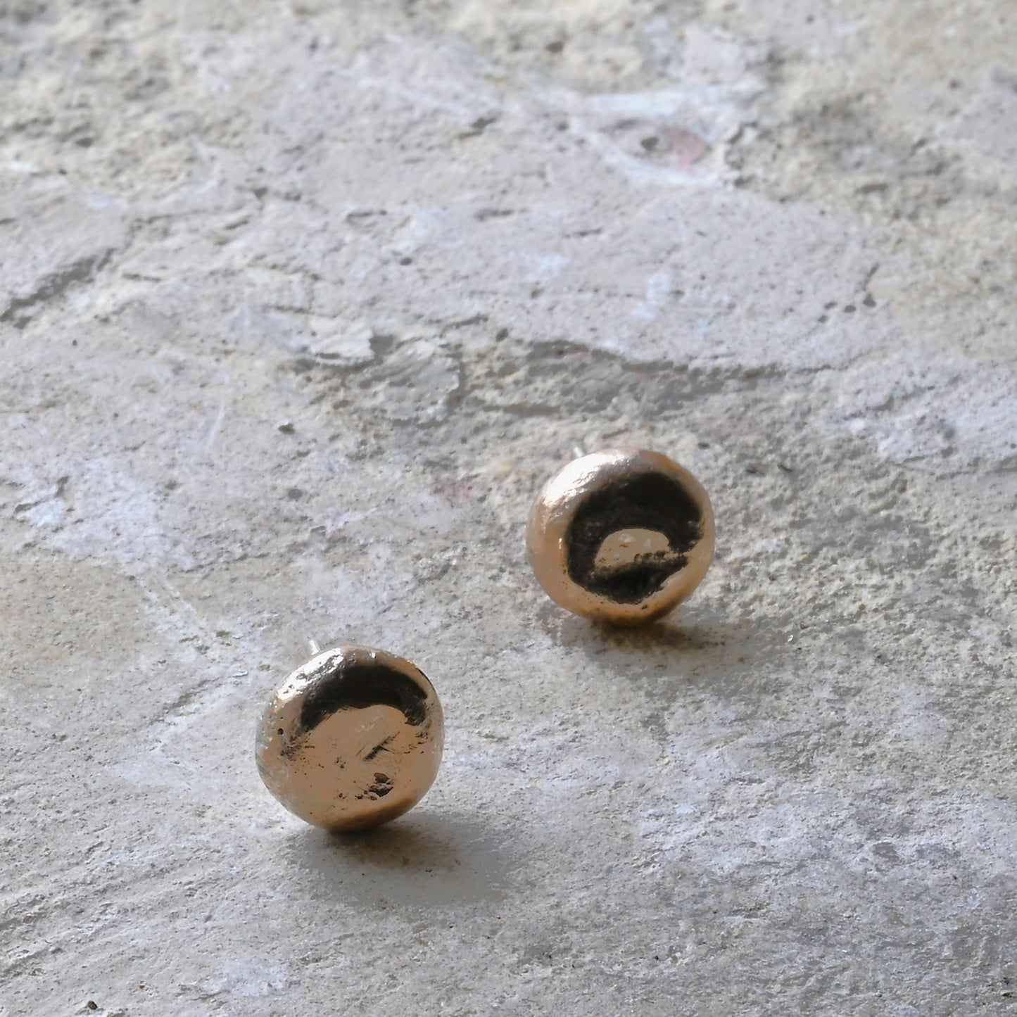 Pair of gold stud earrings on a textured stone surface