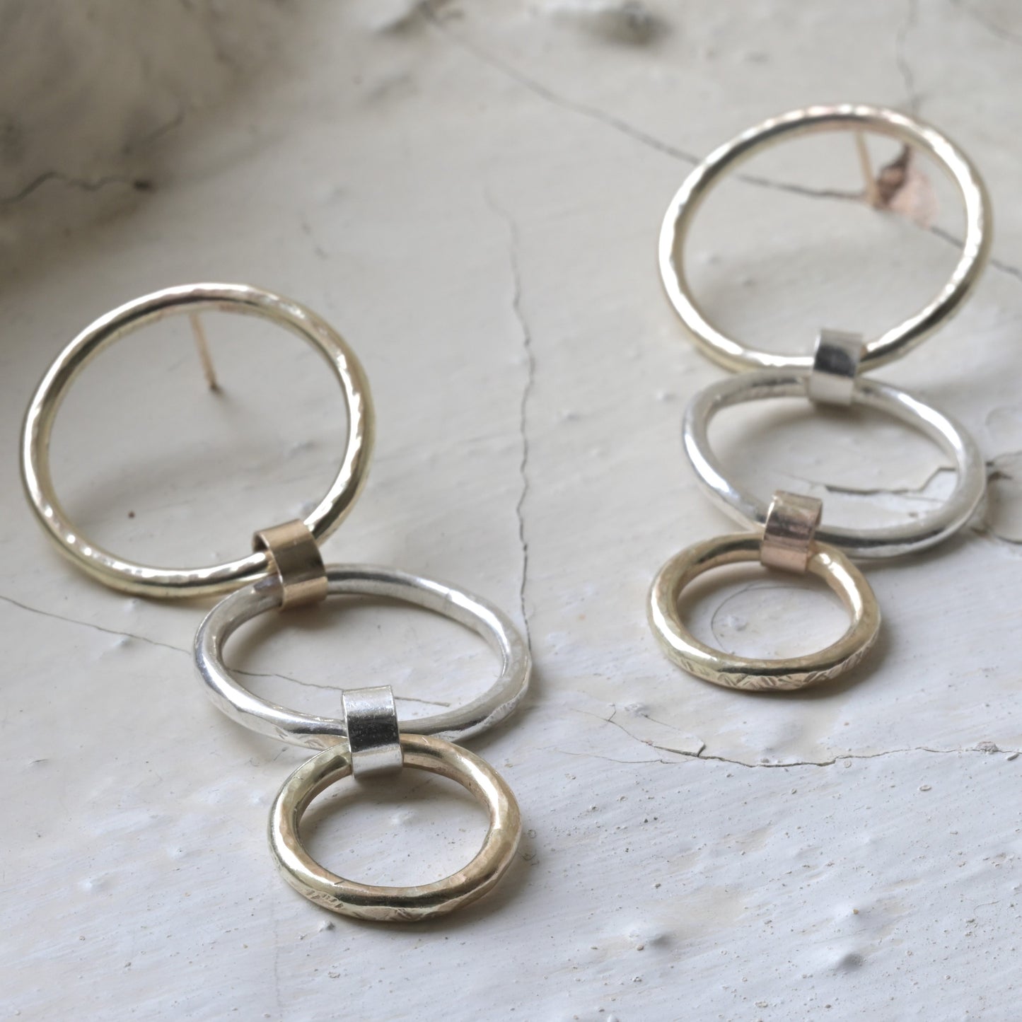 A pair of gold stack earrings with three ascending circles, crafted from sterling silver and 9ct yellow gold, placed on a white surface.