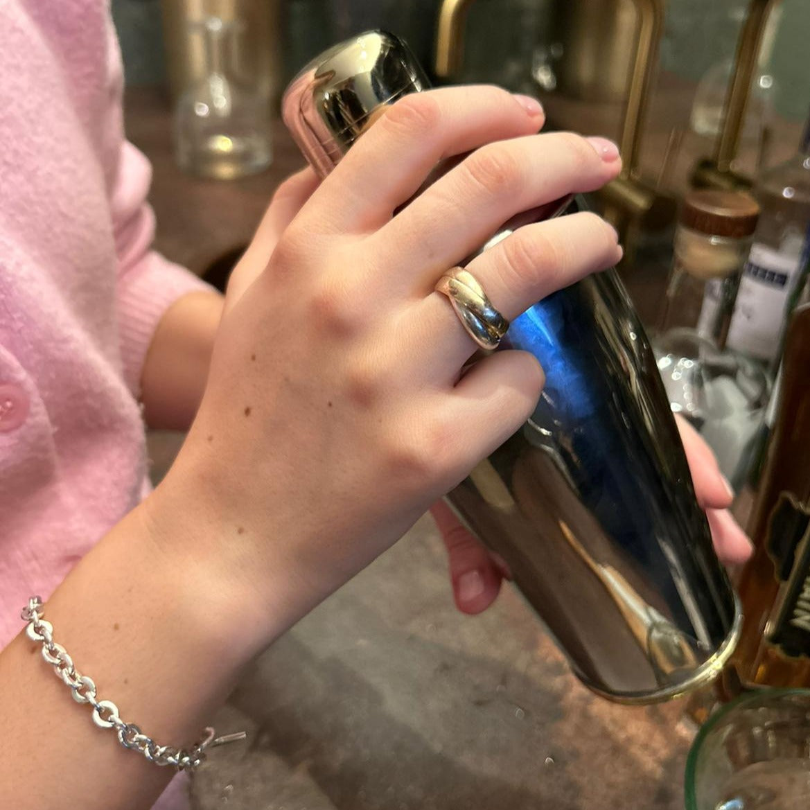 a female making cocktails, holding a cocktail shaker while wearing a handmade 9ct yellow and sterling silver interlocking ring.