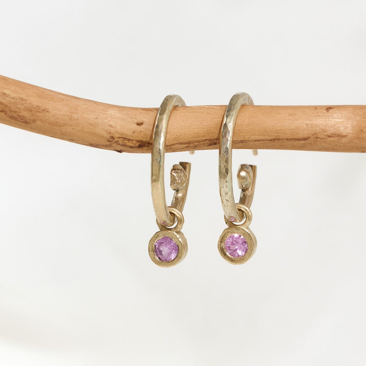 A pair of 9ct yellow gold hoop earrings with sapphire drops, displayed on a wooden branch against a white background.