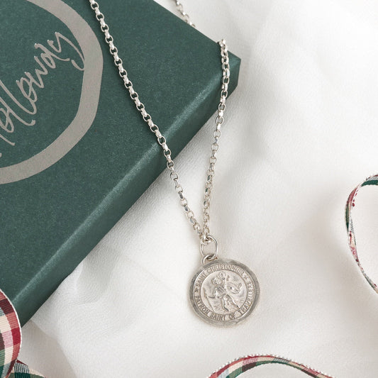 A silver St. Christopher pendant with a diamond-cut belcher chain, displayed on a book and a red-and-white checkered ribbon.