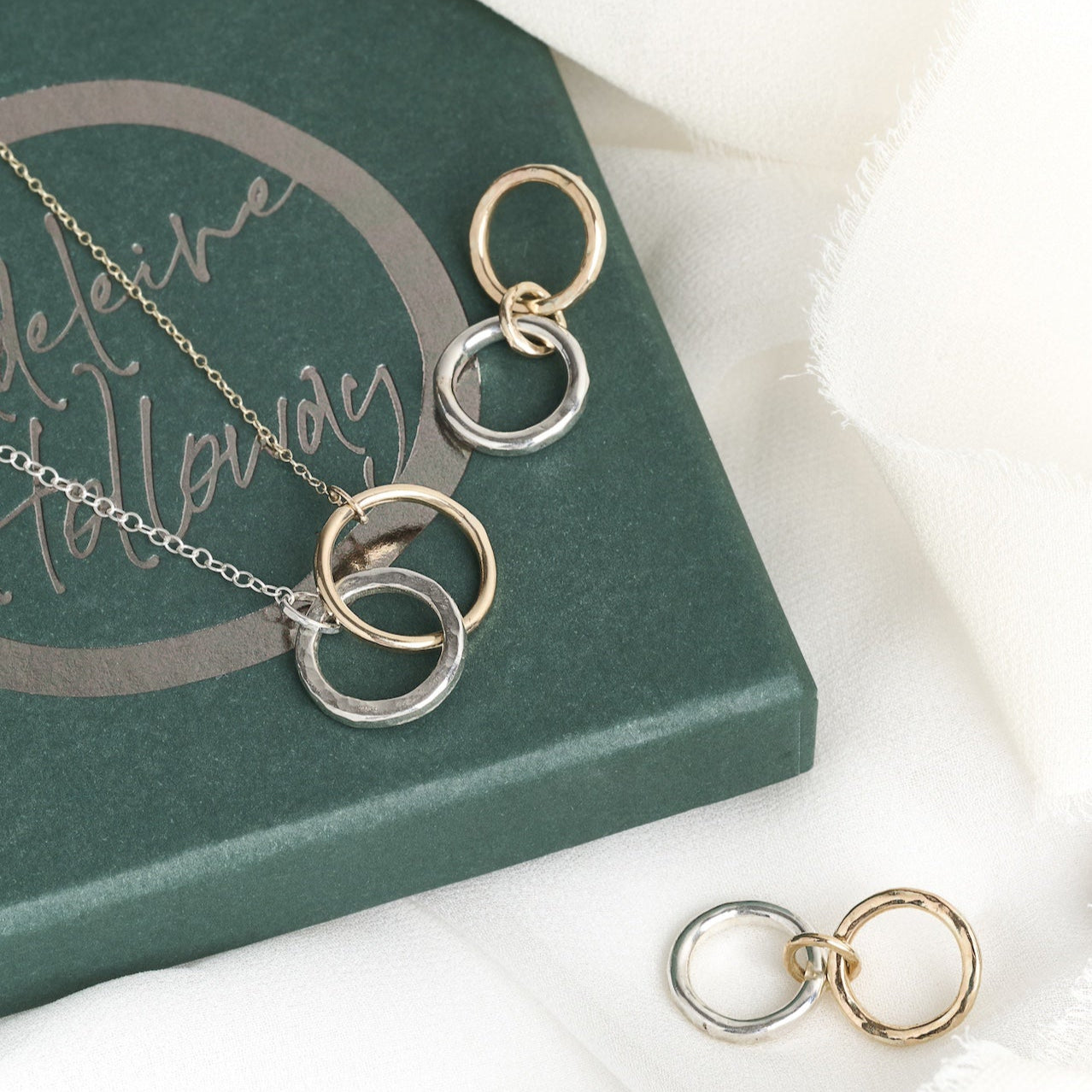 A gold and silver interlocking infinity necklace and earring set displayed on a book with a soft white fabric background.
