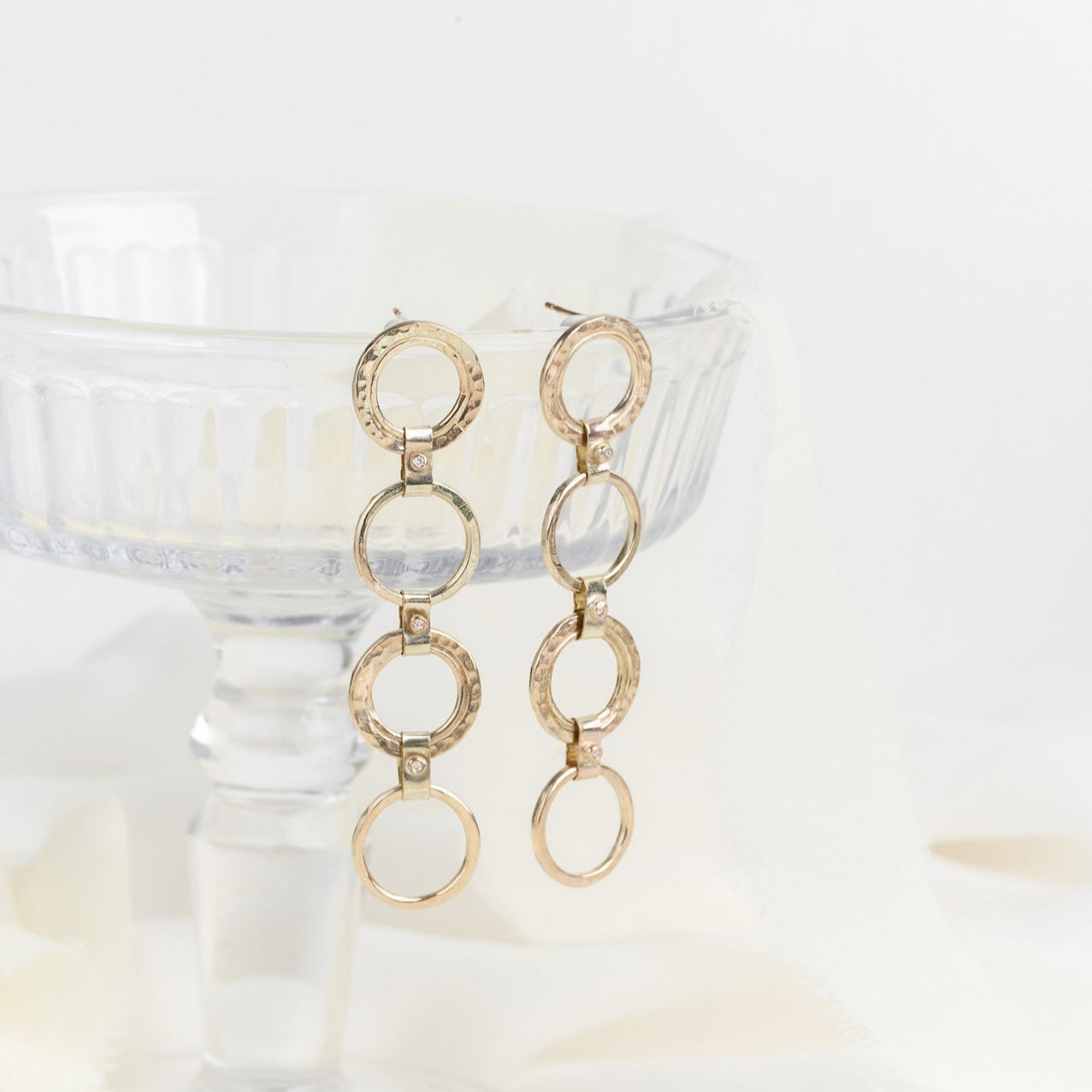 A pair of gold diamond carousel circle drop earrings displayed on a surface with a blurred background.