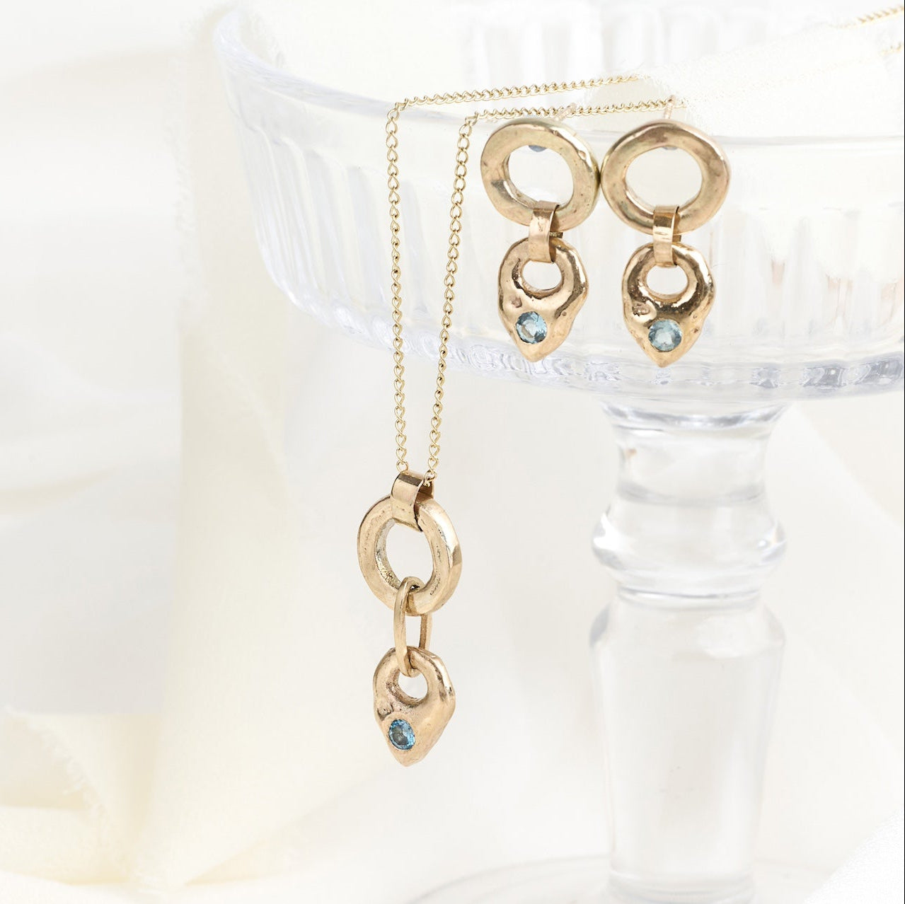Gold earrings with blue gemstones on a clear stand against a white background