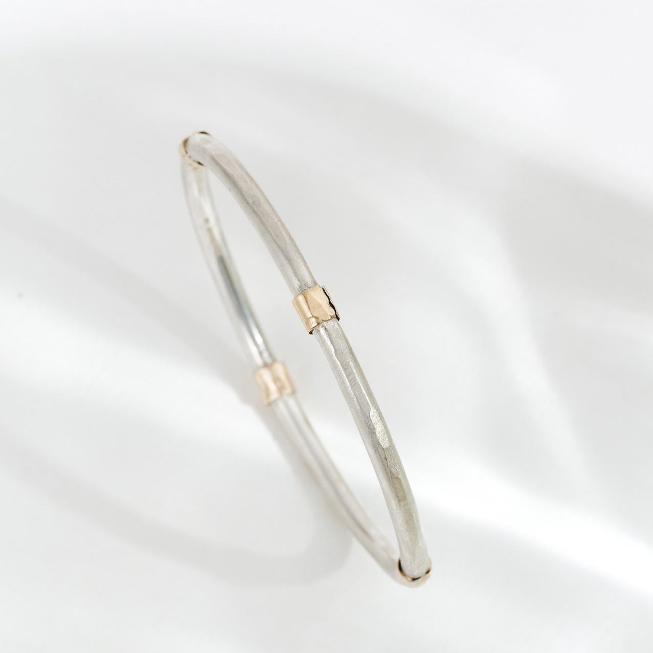 A silver bangle bracelet with patterned details and small gold accents