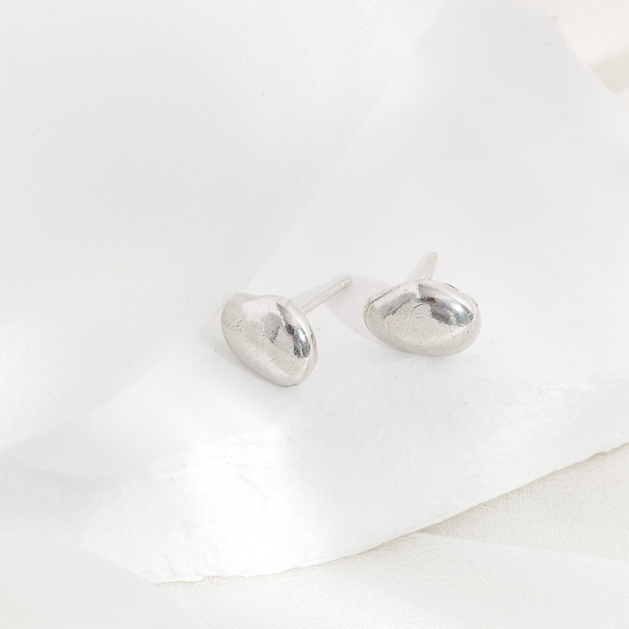 A pair of silver stud earrings placed on a white textured surface.