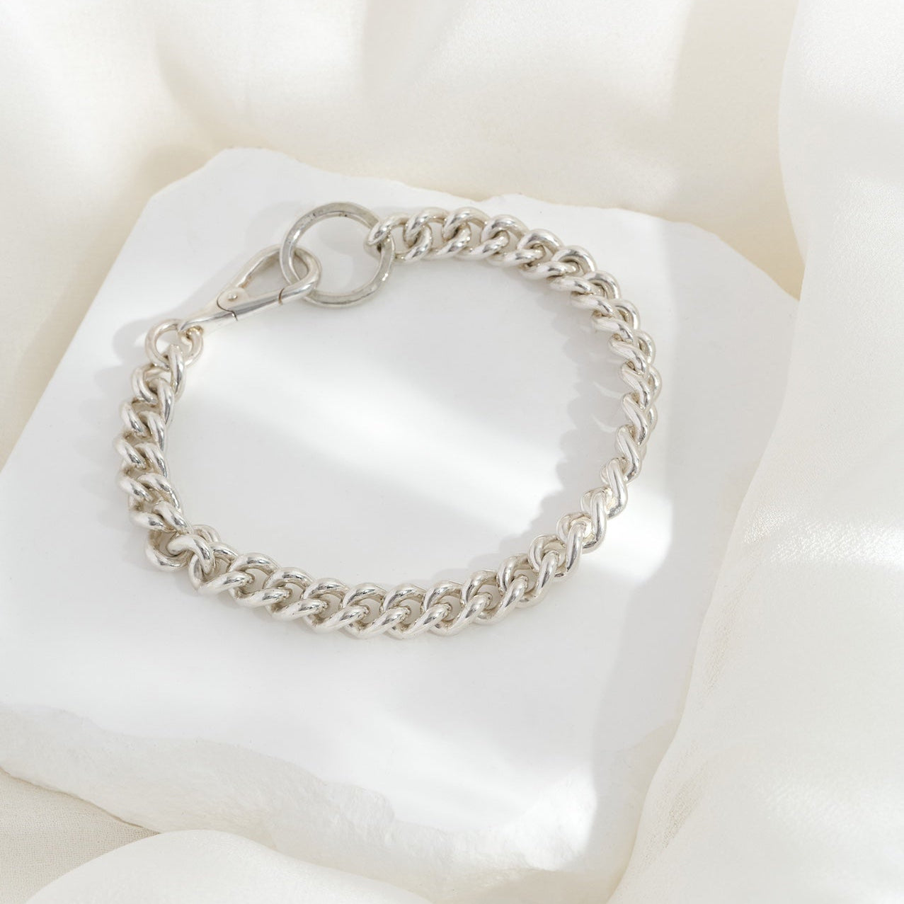 A sterling silver bracelet with a chunky chain design and a lobster catch on a white textured surface.