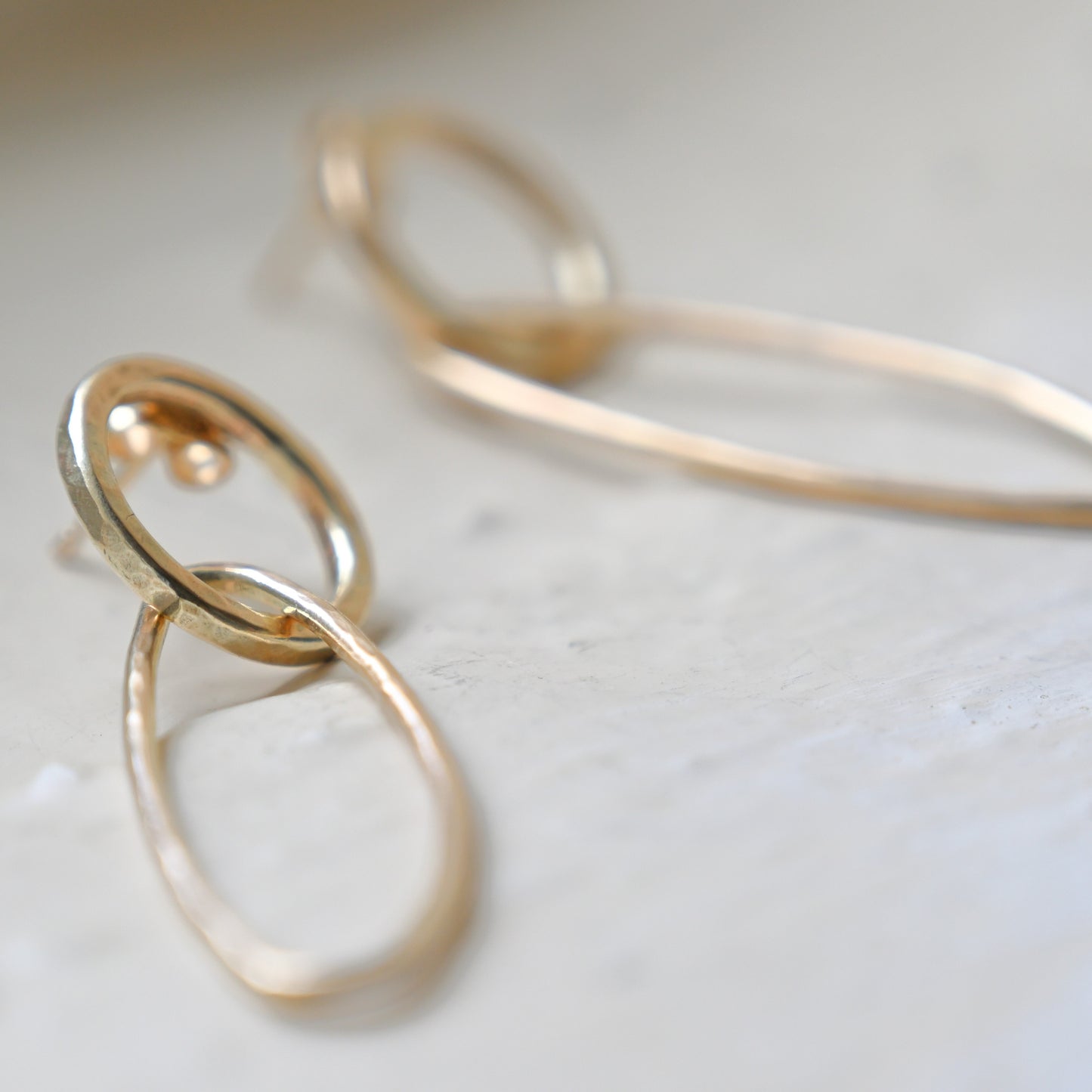 A pair of gold oblong drop earrings laid on a white surface.
