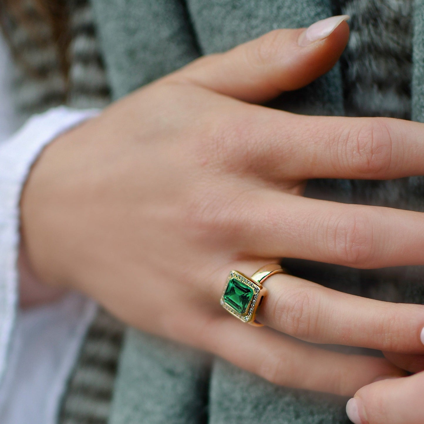 Hand wearing a gold ring with a green gemstone, blurred background