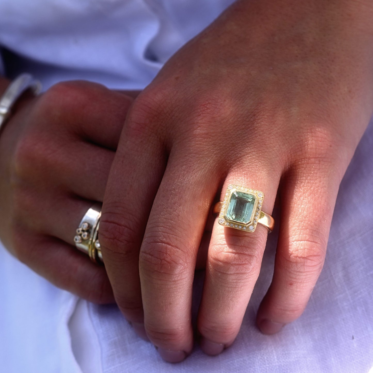 Close-up of a hand wearing a gold ring with a green gemstone on a white background