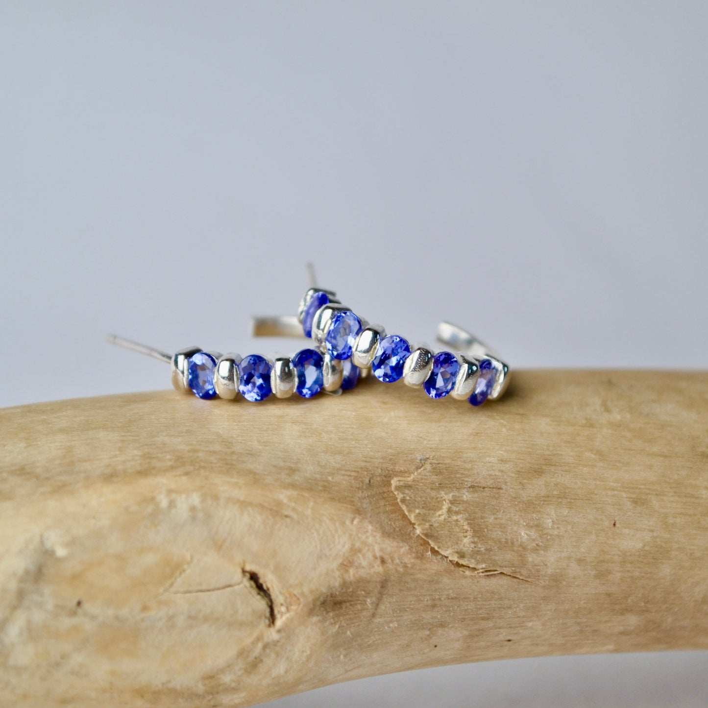 Silver hoop earrings with blue gemstones on a wooden surface