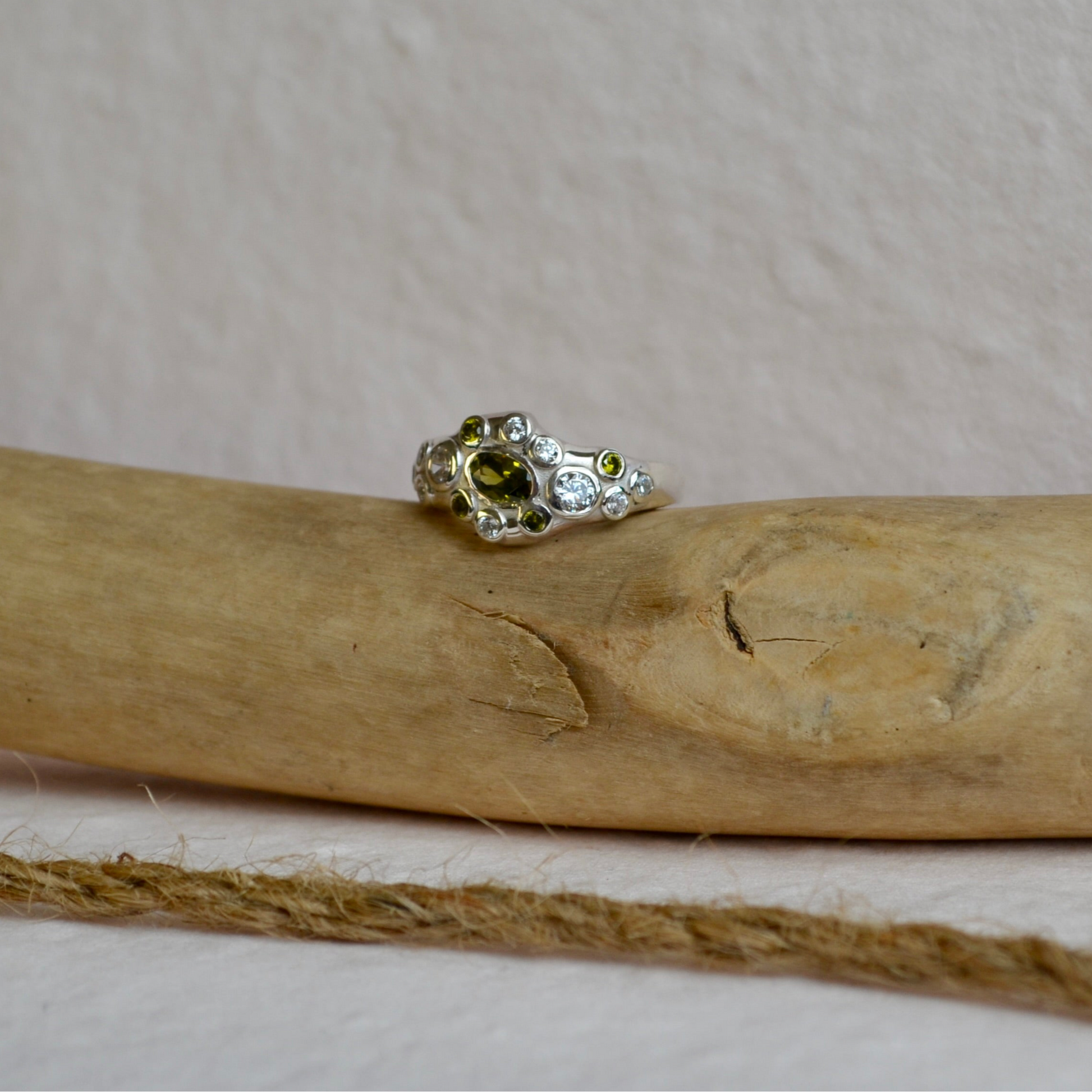 Silver ring with green gemstone on a wooden stick against a beige background