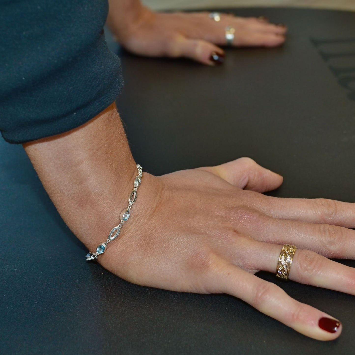 Close-up of a person's hand wearing a bracelet and ring on a dark surface