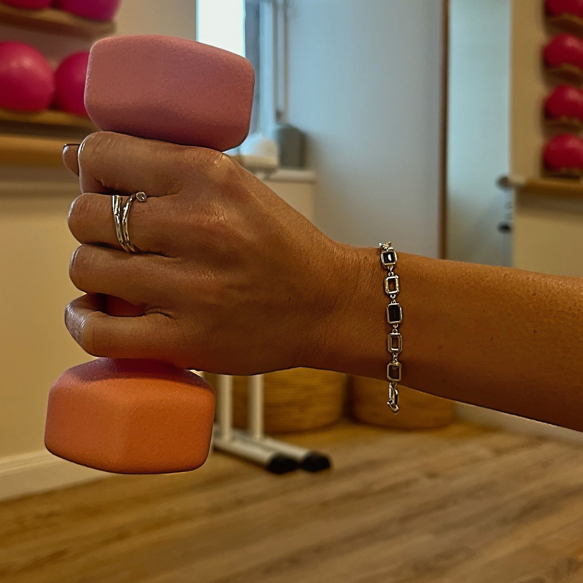 Hand holding a pink dumbbell with a blurred gym background