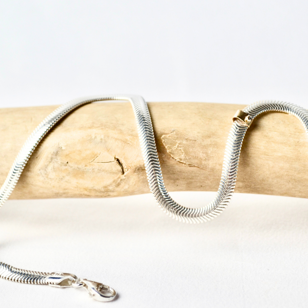 Silver snake chain necklace on a wooden stick with a white background